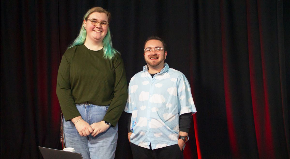 Two people standing in front of red drawn curtains smiling to the camera.